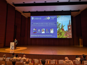Dr Max, standing on the Nido2026 stage presenting the labs work on MHV replication